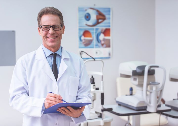 Oftalmólogo sonriente escribiendo notas de consulta de cirugía de cataratas en la Clínica Láser de Ojos Medellín