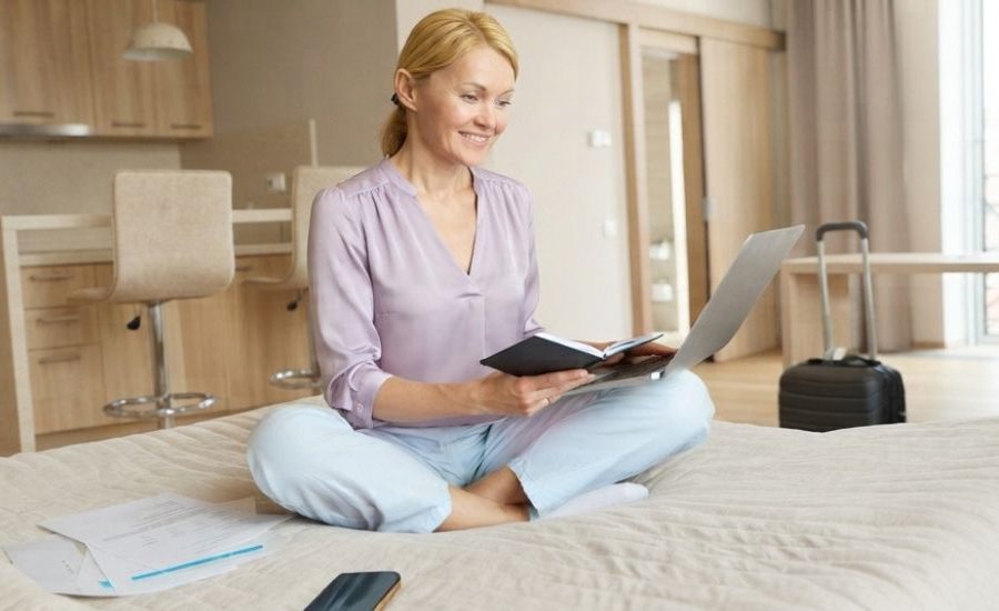 Mujer sonriente organizando su viaje médico en una habitación de hotel con su laptop, preparándose para una cirugía ocular en la Clínica Láser de Ojos Medellín.